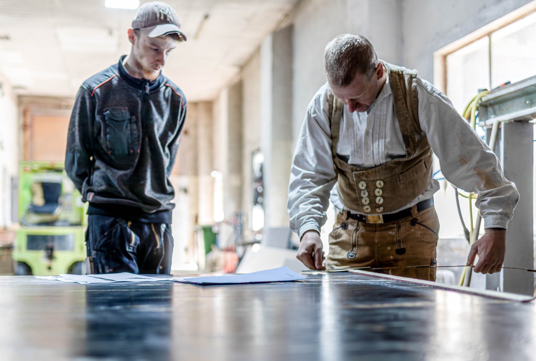 Zwei Handwerker besprechen die Bearbeitung einer Steinplatte in der Werkstatt